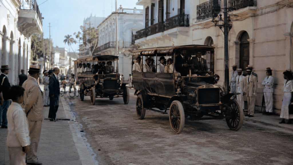 Early automobiles on a historic Dominican street, representing the arrival and expansion of motor vehicles in the Dominican Republic
