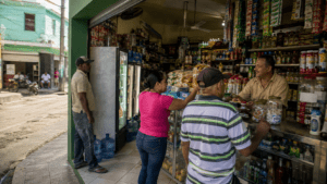 A Dominican colmado serving customers in a neighborhood with shelves of everyday groceries and beverages