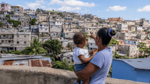 Dominican woman holding a child and overlooking a densely populated urban neighborhood in the Dominican Republic