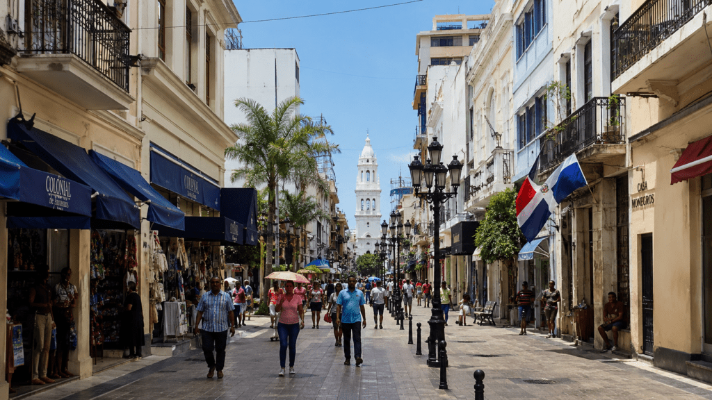 Calle peatonal de la Zona Colonial de Santo Domingo con edificios históricos, comercios y personas caminando bajo el sol