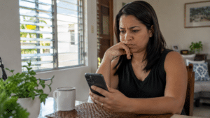 Dominican woman examining an unexpected message on her smartphone at home, illustrating mobile phone scams and cybersecurity risks in the Dominican Republic